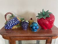 Front view of all five ceramic fruit-themed containers displayed on a wooden table