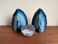 Front view of blue agate geode bookends with smaller geode stone between them on wooden surface.