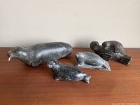 Four indigenous soapstone figurines displayed on a wooden surface, showing size and condition.