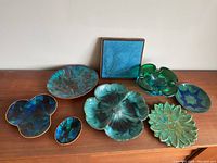 Photo of eight ceramic decorative plates and dishes in various shapes and related colors arranged on wood surface.
