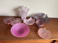 View of all seven pink glassware pieces arranged on a surface showing their shapes and colors.