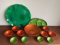 Full overview of the serving dish set including large green plate, green leaf-shaped dish, large orange bowl, four small orange bowls, and three small green bowls.