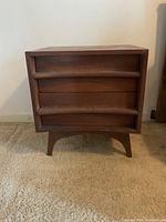 Front view of the wooden side table showing three curved front drawers with horizontal integrated handles and tapered legs.