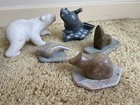 Photo of five stone animal sculptures on carpeted floor showing a polar bear, duck, small bird on base, black bird on polka dot base, and heart-shaped stone on base.