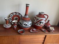 Full set of 8 Ukrainian ceramic pottery items displayed on a wooden sideboard including vases, jug, plate and decorative items all hand painted with black and white animal motifs on terracotta background.