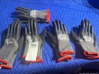 Five pairs of Milwaukee gloves laid on a blue protective pad. Gray knit gloves with black rubber grip and red wrist trim visible.