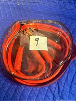 Clear image of new unopened red booster cables bundled and sealed in plastic wrapping, showing metal clamps with red rubber handles.