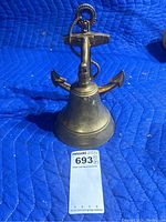 Frontal view of the brass nautical bell with anchor motif standing upright on a blue padded surface. Seller's lot tag included for size reference.