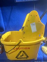 Yellow commercial mop bucket with wringer, caution label on side, and metal handle.
