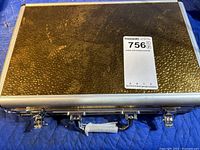 Closed metallic silver carrying case with latches and handle wrapped in tape.