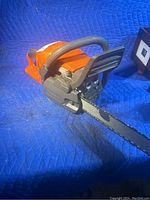 Side view showing orange housing, front handle and guide bar with chain