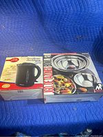 Photo showing boxed Betty Crocker electric kettle and boxed five-piece stainless steel mixing bowl set on a blue background.