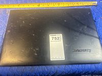 Top view of the closed black Lenovo laptop showing exterior lid with scratches and a MaxSold lot sticker.