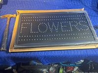 LED sign showing 'FLOWERS' in unlit bulbs on black background, packaged and new.