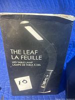 The leaf LED table lamp packaging box which is black with some wear, showing a photo of the lamp and product name in English and French.