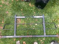 Pickup truck back rack frame placed on grass surface with visible horizontal bars and mounting holes.