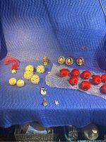 Full overview of all assorted vintage Christmas ornaments laid on a blue quilted surface, including red glass balls, foil balls, flower style ornaments, snowman and bell ornaments.