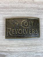 Full view of the rectangular Colt Revolvers belt buckle on wooden surface.