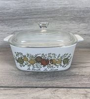 White rectangular Corningware casserole dish with a clear glass lid on a wood background, showing front side botanical artwork and lid attachment.