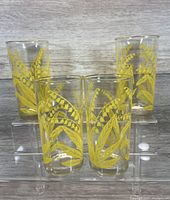 Set of four clear glass tumblers decorated with yellow floral pattern, displayed on clear risers.