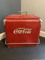 Front view of red Coca-Cola metal cooler showing 'Drink Coca-Cola' logo and metal handle on lid.