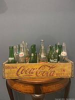 Front view of Coca Cola wooden crate filled with an assortment of glass soda bottles from different brands including Coca Cola, Pepsi, Hires, and Rummy.