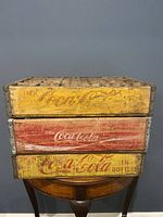 Front view of three stacked vintage Coca Cola wooden crates, showing worn yellow and red painted logos.
