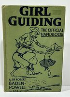 Front cover of the green hardcover book titled 'Girl Guiding The Official Handbook' with illustrated figures and author name.