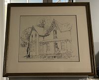 Framed pen and ink drawing showing a farmhouse with detailed roofline and porch under glass and within a gold-tone frame.