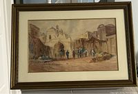 Frontal view of the framed watercolour painting showing street scene with domed buildings, people, and camels.