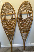 Full view of pair of vintage Canadian wooden snow shoes with woven webbing hanging on wall showing size and style.