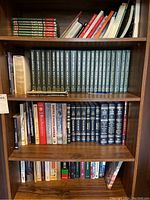 Full view of two shelves containing Lexicon Universal Encyclopedia volumes in dark blue and various other hard and soft cover books mostly about nature and biology.