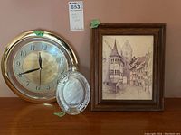 Photo of the gold-tone wall clock, glass-covered, along with the silver decorative mesh tray and framed print.