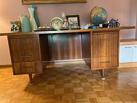 Front view of wood desk showing three drawers on left side and one drawer on right side, flat top surface with decorative items (not included)