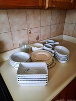 Photo showing the full set of dishes including pie dishes, soup bowls, plates, and glasses arranged on a kitchen counter.