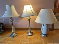 Wide shot showing the three lamps placed on floor against wall, two matching lamps on left and one white ceramic lamp on right.