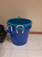 Two large blue plastic buckets stacked with visible white rope handles attached to each bucket.