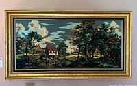 Full view of the framed needlepoint depicting a rural landscape with house, trees, and pond.