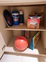 Shelf with boxed pasta maker, blue and white thermoses, metal and plastic trays