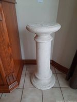 Front view of white plaster pedestal showing round top and cylindrical body.