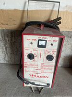 Front view of Vulcan 60202 battery charger showing controls, brand logo, and attached cables on wheels.