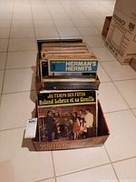 Two boxes filled with vinyl records, showing top album 'The Best of Herman's Hermits' and 'Roland Lebrun et sa famille'.
