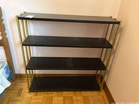 Front view of the black metal shelving unit with brass supports, showing all four shelves.