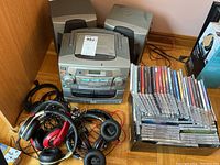 Overview of stereo system with attached detachable speakers, several headphones laid in front, and a stack of CDs on the right.