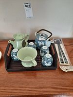 Full view of the tea service set arranged on the wooden tray showing the teapot, two tea cups, light green mug, and packaged chopsticks.