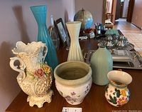 Photo of six ceramic and pottery items on a table including vases, a pot, and a pitcher with various decorative patterns.