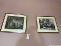 Photo of two framed vintage prints hanging side by side on a wall, titles 'The Young Mother' and 'The Village Doctor' visible under the glass frames