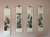Four narrow fabric wall hangings lined up side by side on a wall, each depicting a different mountain and nature scene in an Asian painting style.