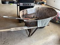 Metal and wood wheelbarrow visible from the side showing wooden handles and weathered metal body, with rag draped over one handle