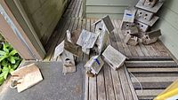 Photo showing most of the birdhouses grouped on a porch floor, varying sizes and designs, all weathered wood.
